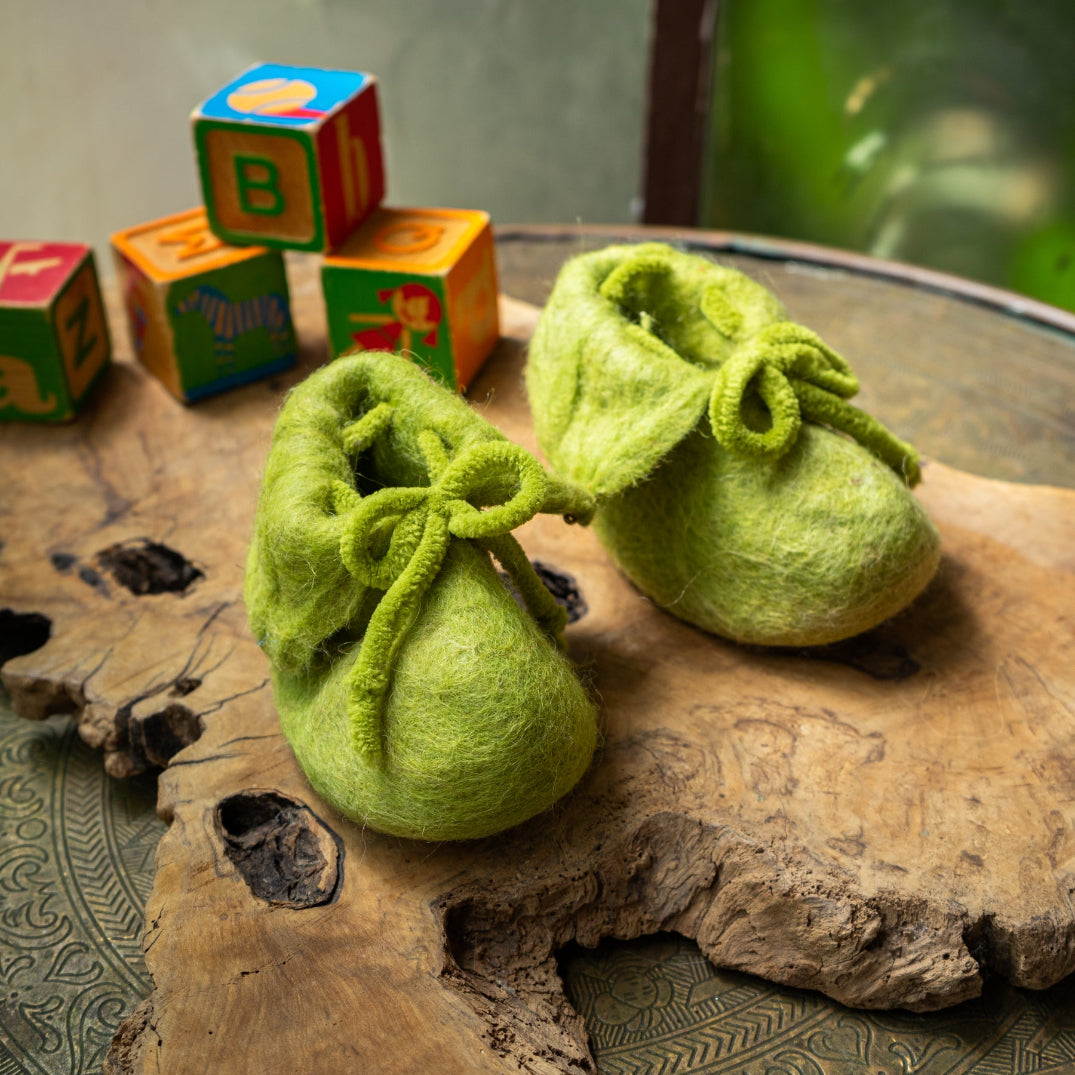 Green baby shoes on a wooden surface with colorful blocks in the background