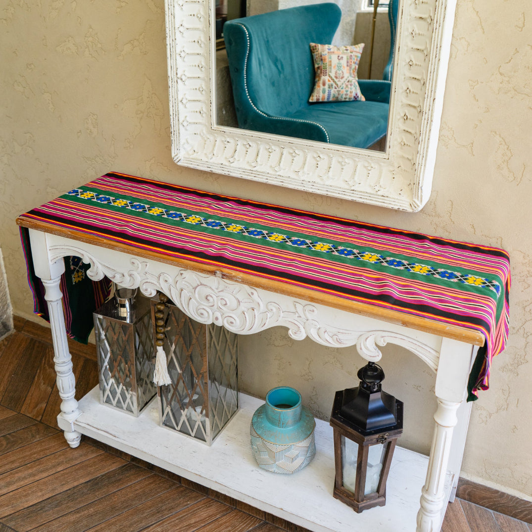 Decorative table runner from Syrian Majdalawi fabric with colorful stripes and Palestinian tatreez, mirror, and decorative items in a room.