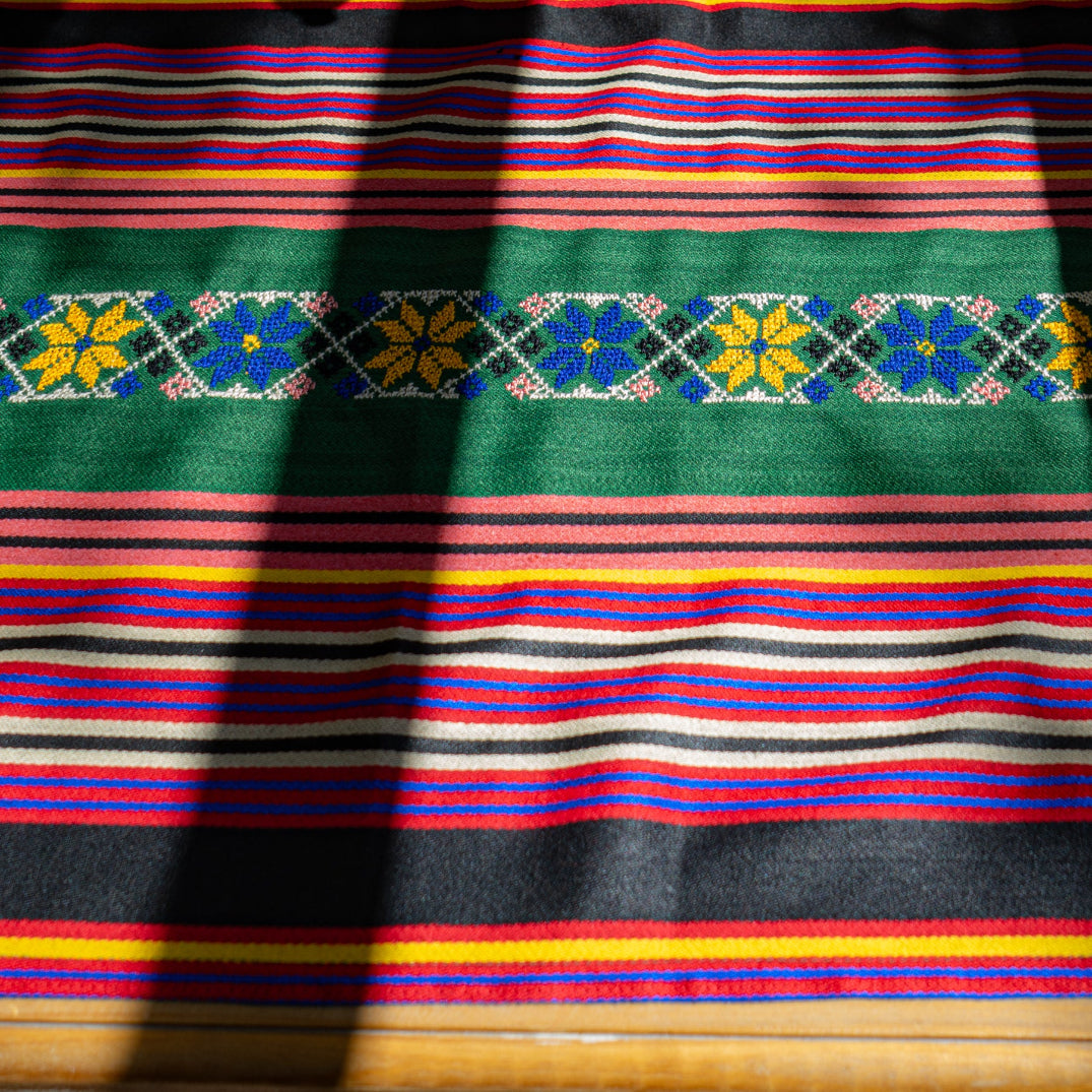 Syrian striped majdalawi fabric with tatreez floral patterns on a wooden surface