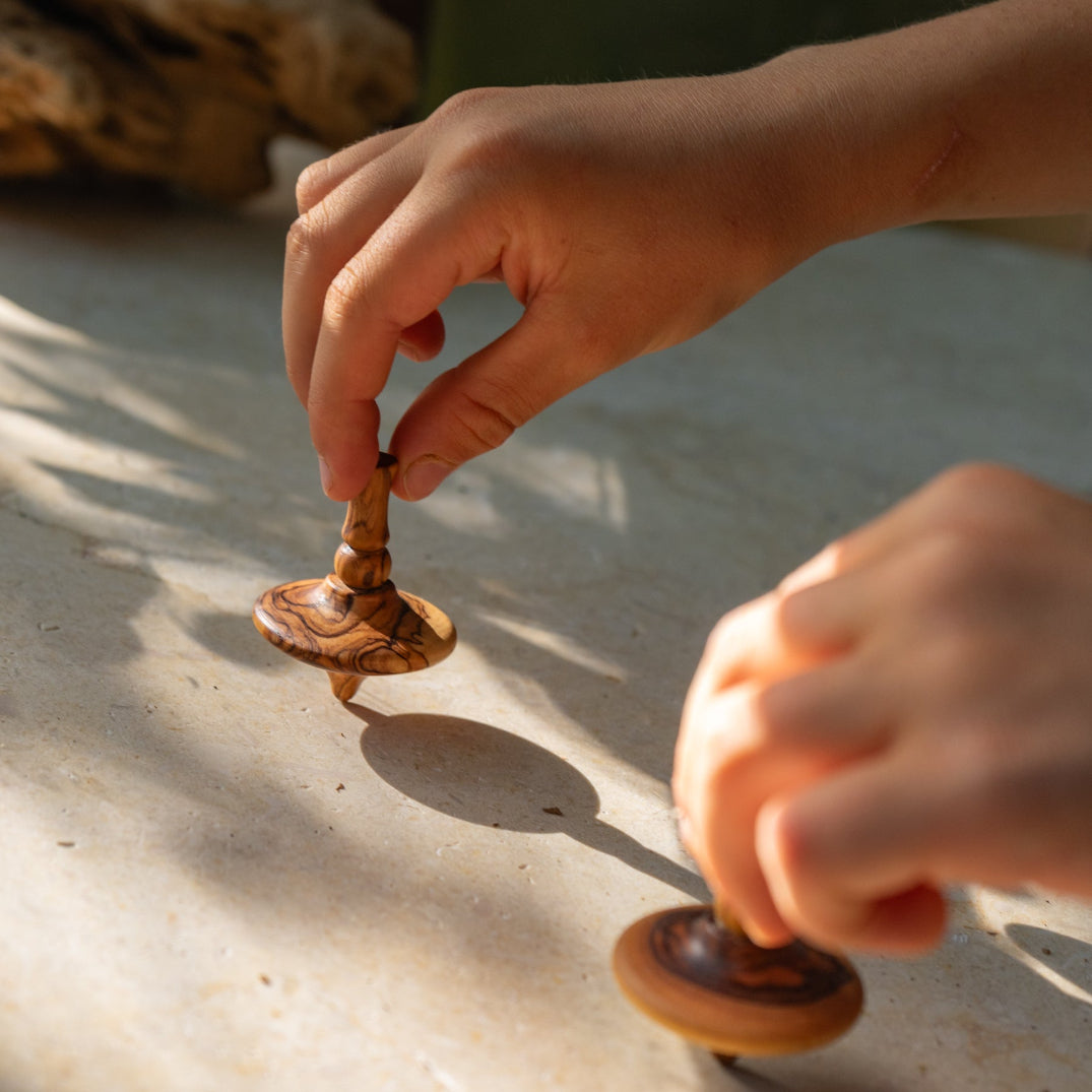 Child's hands playing with olive wood spinning top on a sandy surface