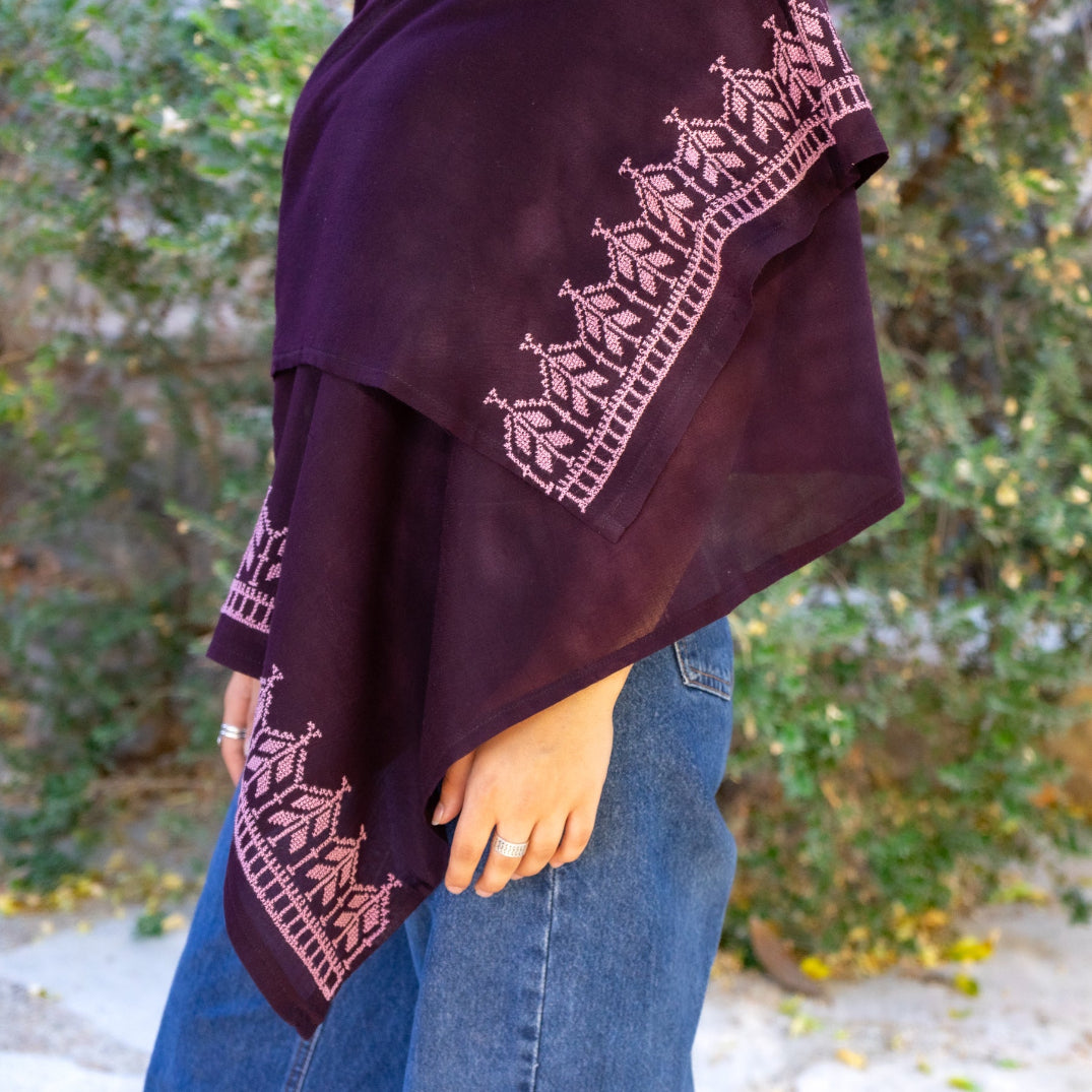 Palestinian woman wearing a dark purple shawl with lavender embroidery against a natural background