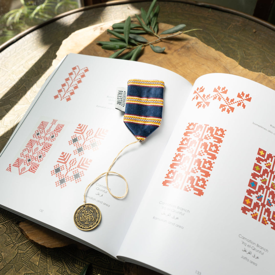 Open book with embroidery patterns and a decorative item on a wooden surface
