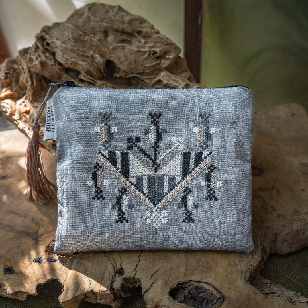 Silver pouch with Palestinian tatreez in Gaza pattern on a natural stone background