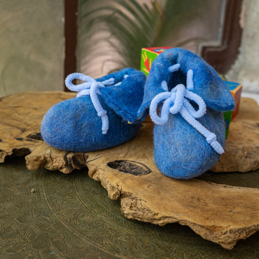 Pair of blue baby booties in hand felted wool with light blue laces on a wooden surface.
