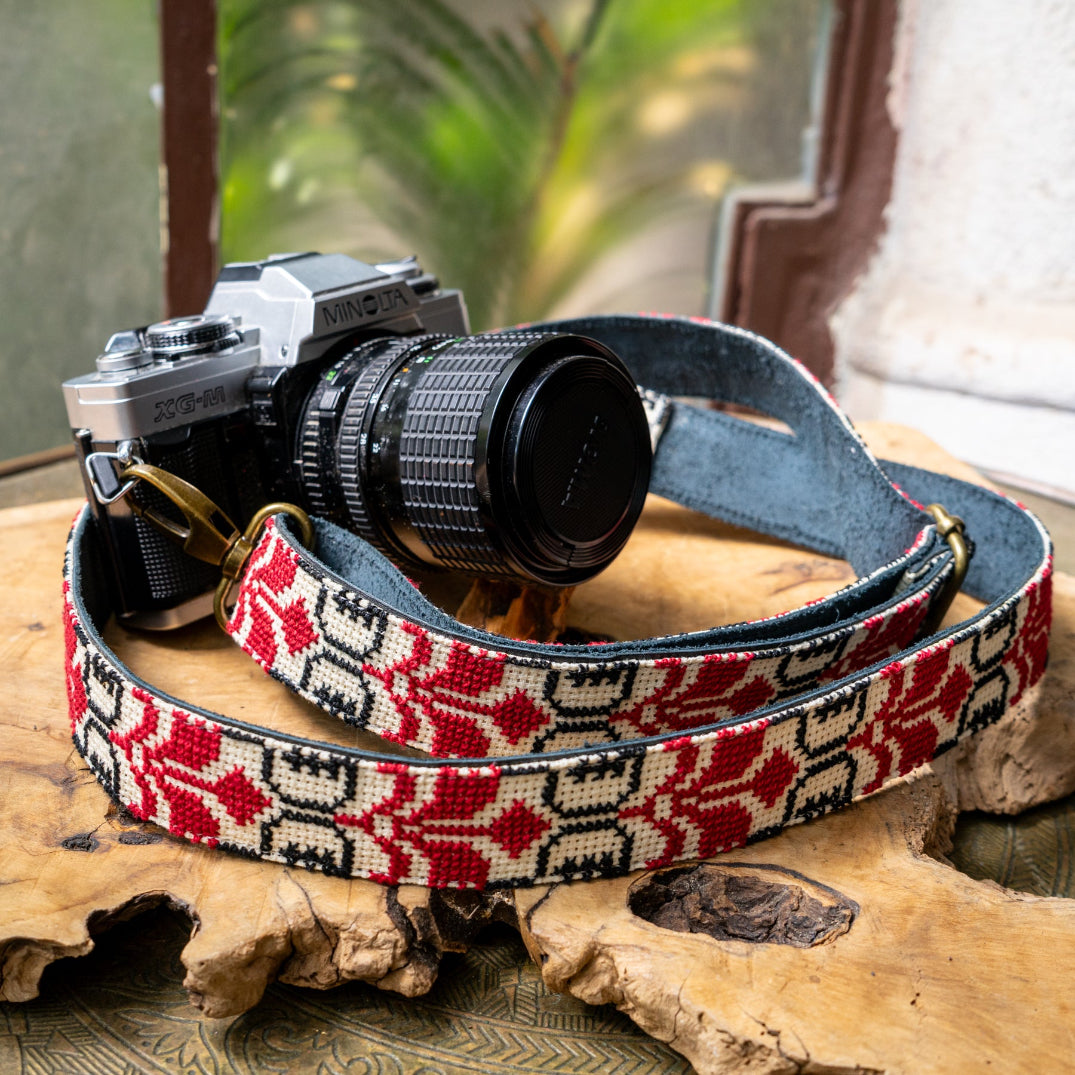 Camera with a patterned tatreez strap and black leather backing on a wooden surface