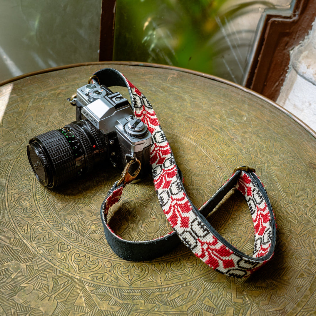 Camera with a red and black patterned strap on a textured surface