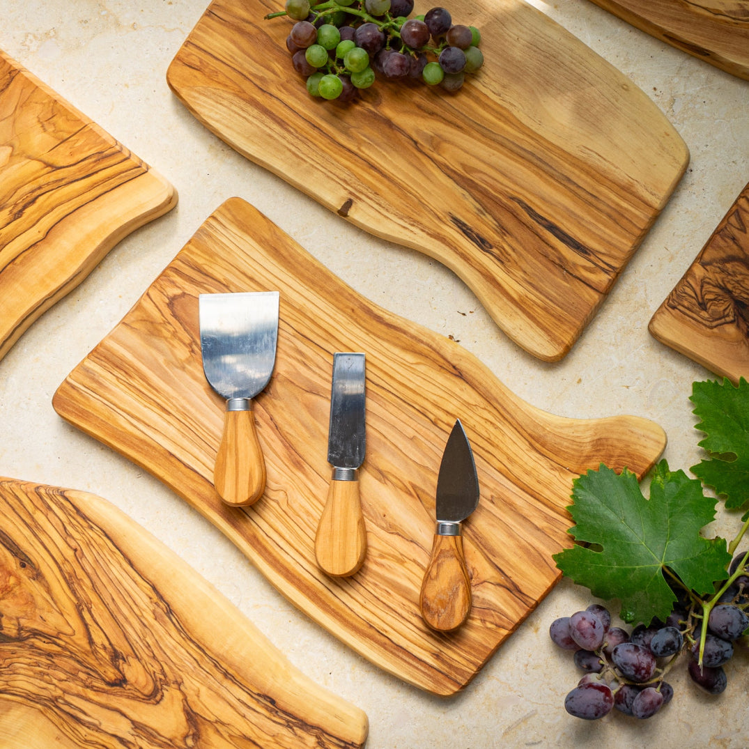 Olive wood hand crafted cutting boards with cheese knives and grapes on a light surface