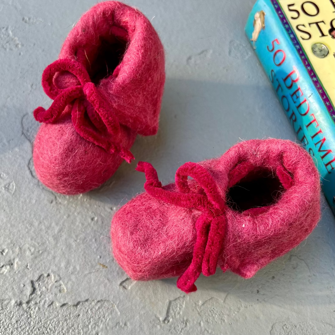 Pair of pink baby booties on a textured surface with a book titled '50 Bedtime Stories' in the background.