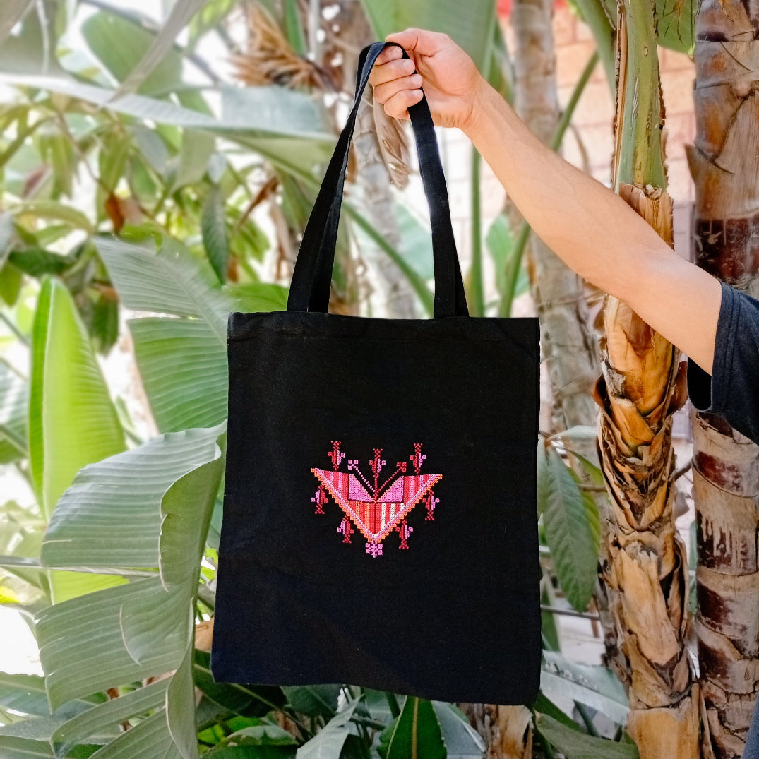 Black tote bag with pink and red design held by a person against a natural background