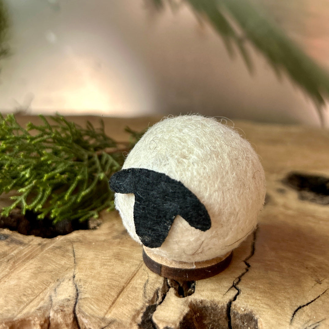Felted wool small sheep figurine on a wooden surface with greenery in the background