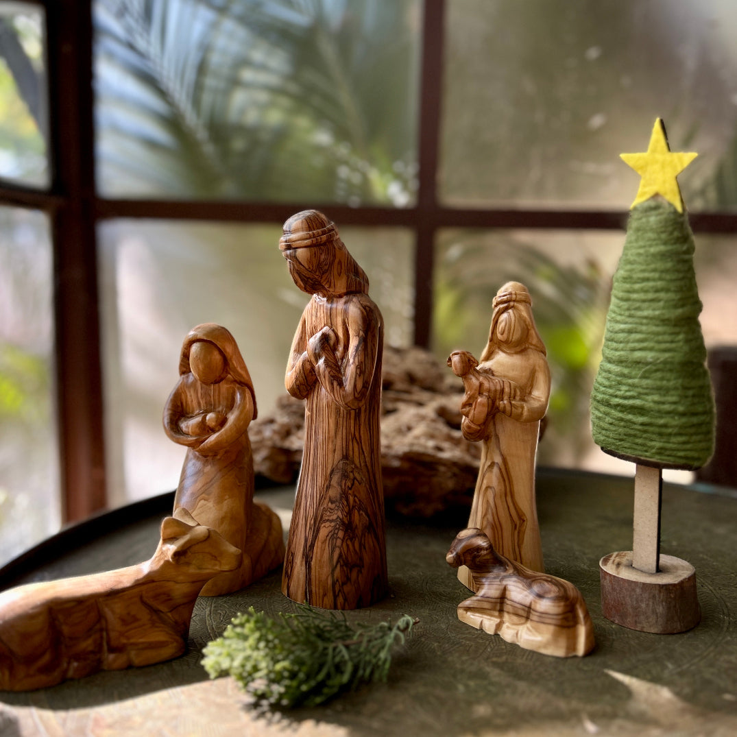 Hand carved olive wood nativity scene figures with a small tree on a windowsill.