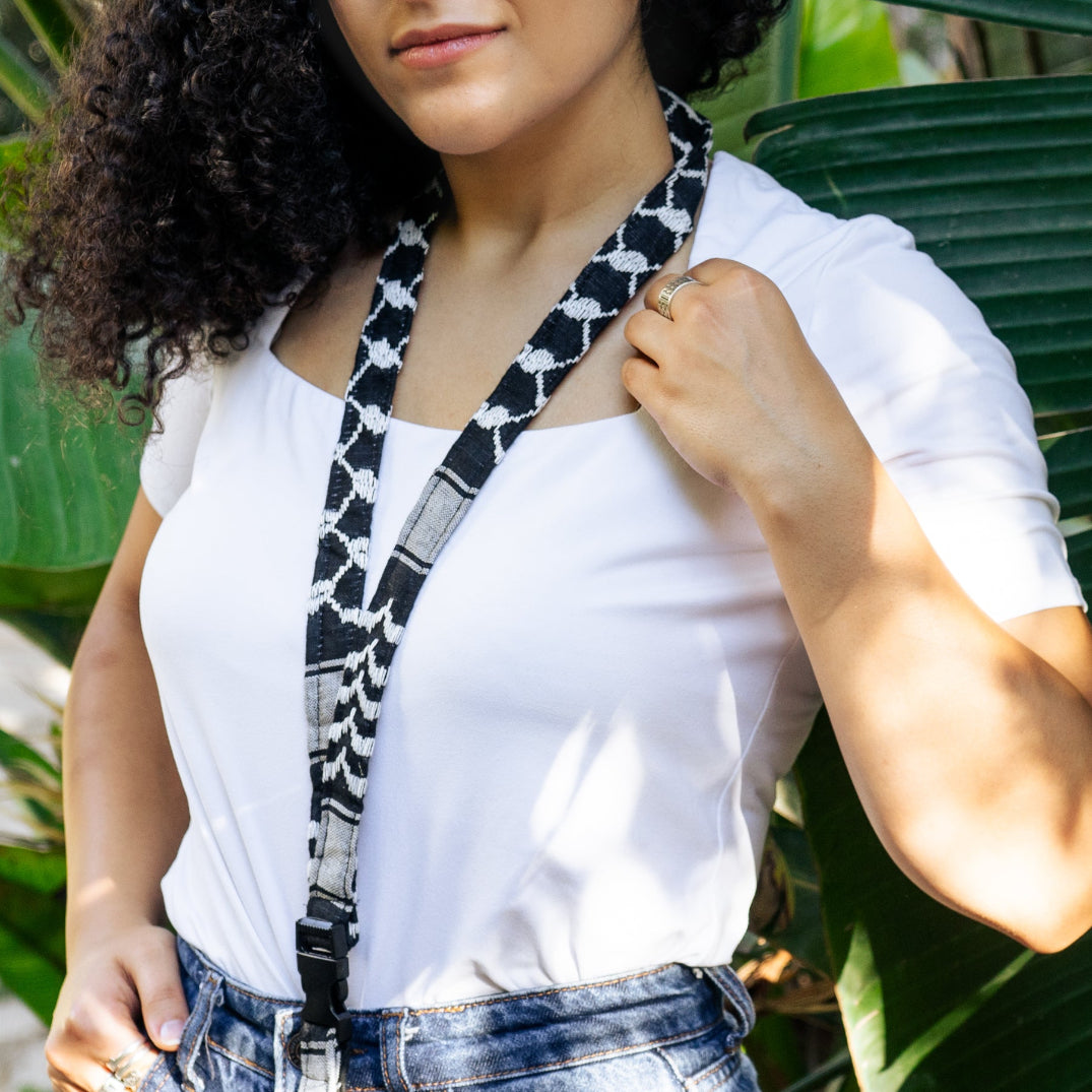 Palestinian woman wearing a keffiyeh patterned lanyard, standing in front of green foliage.