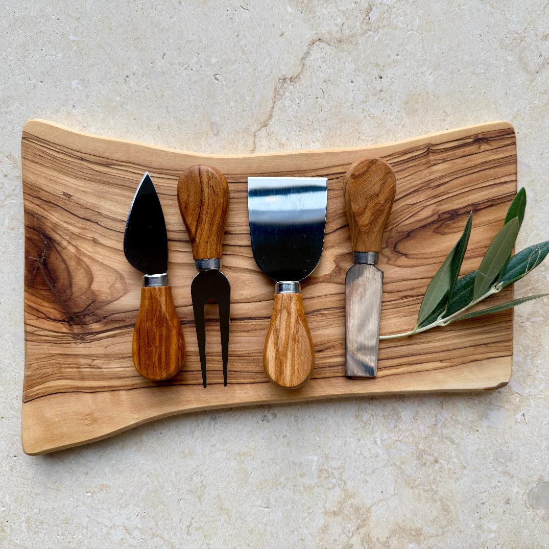 Set of cheese tools on an olive wood cutting board with a light background