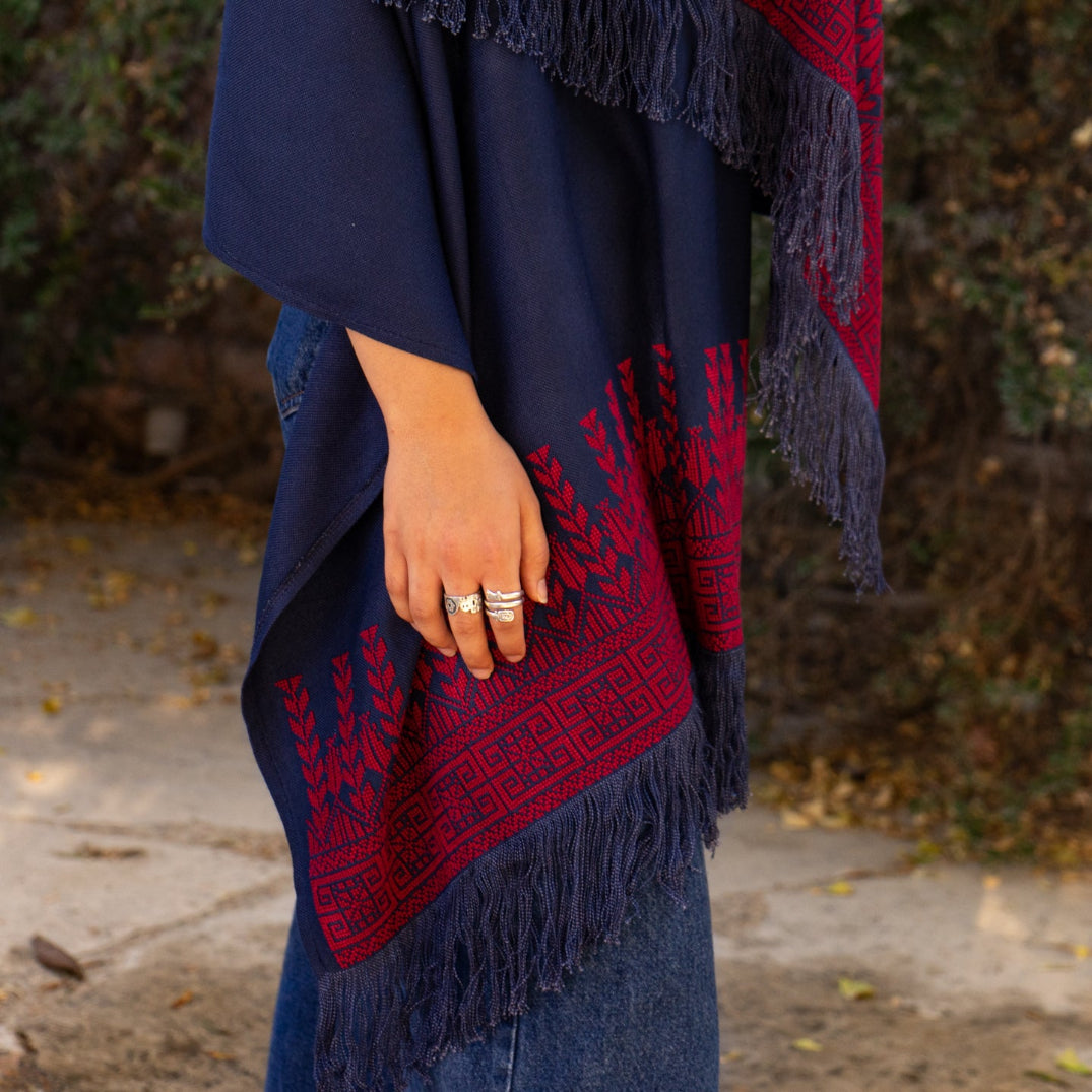 Navy blue and red patterned shawl with fringe held by a person outdoors.