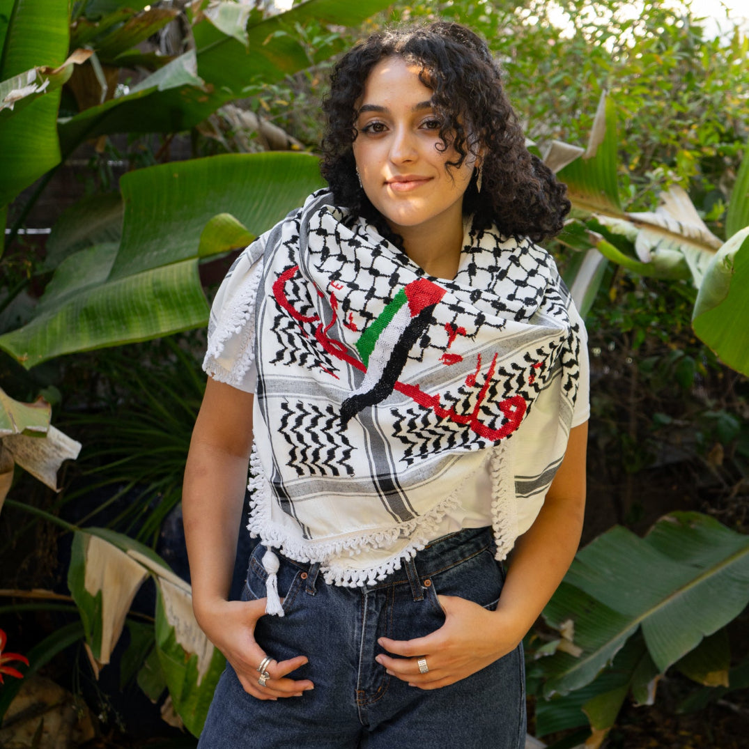 Palestinian woman wearing a Palestinian flag tatreez keffiyeh in a natural setting