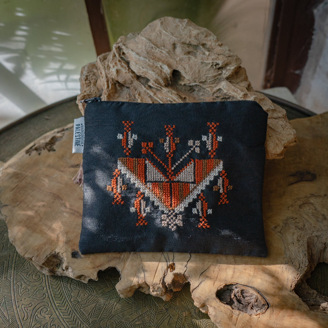Embroidered fabric pouch with Palestinian tatreez on a natural stone surface