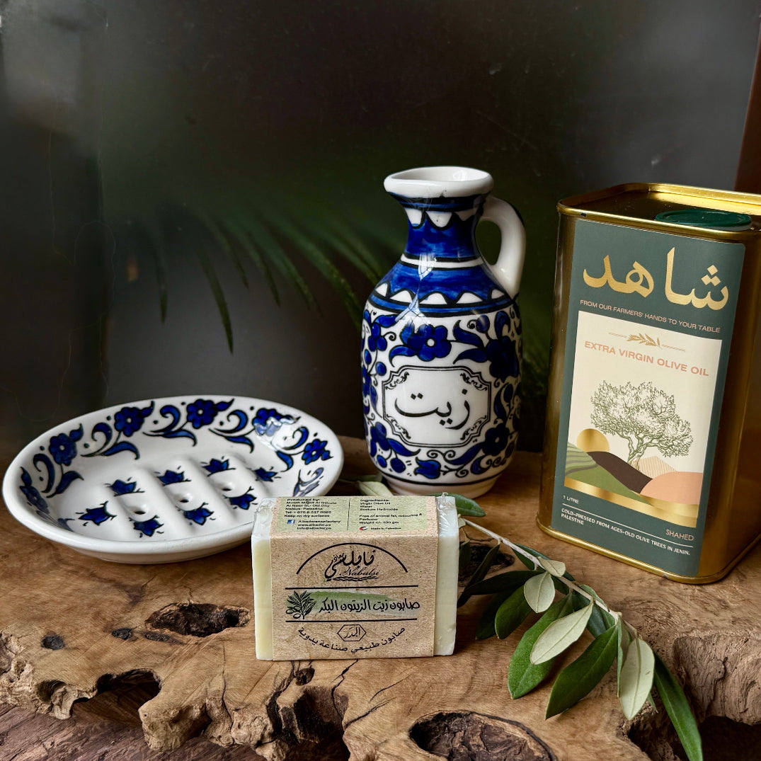 Decorative items including a blue and white ceramic pitcher, soap, and olive oil packaging on a wooden surface.