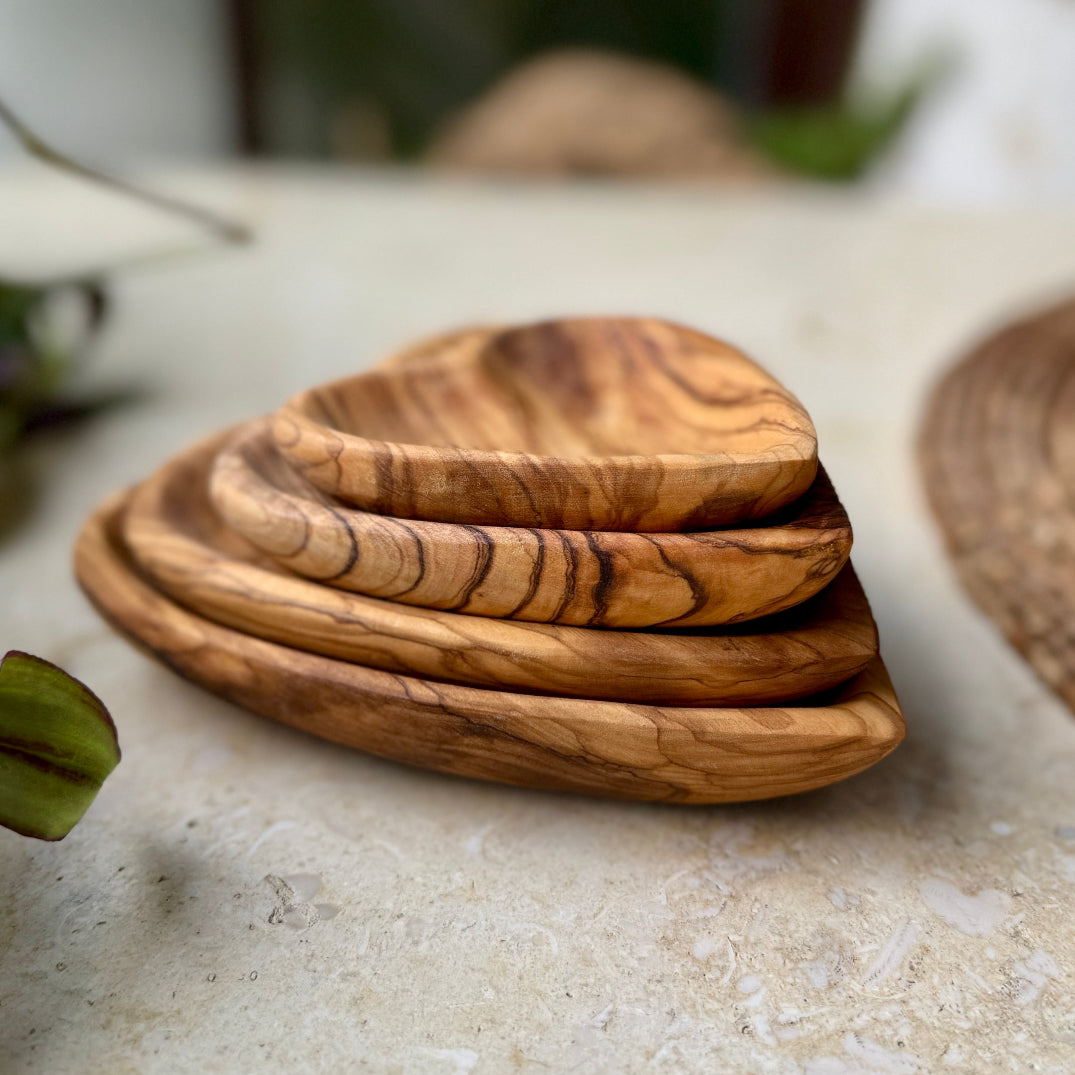 A stack of four nested olive wood serving plates with a prominent natural grain pattern, resting on a light beige stone surface.