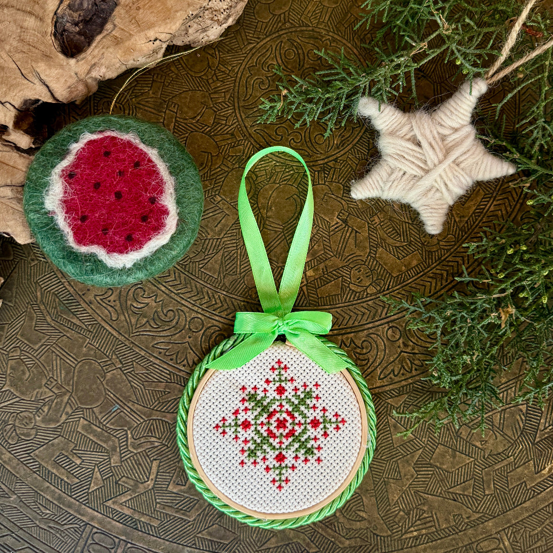 Decorative ornament with cross-stitch design on a textured surface with greenery