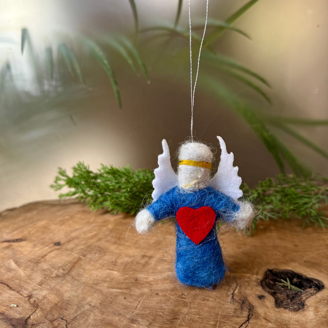 Decorative angel ornament with a red heart on a wooden surface with greenery in the background