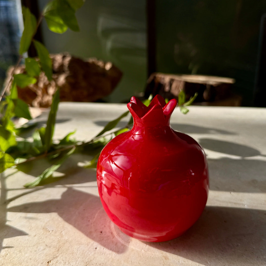 Red decorative object resembling a pomegranate on a stone surface with plants in the background