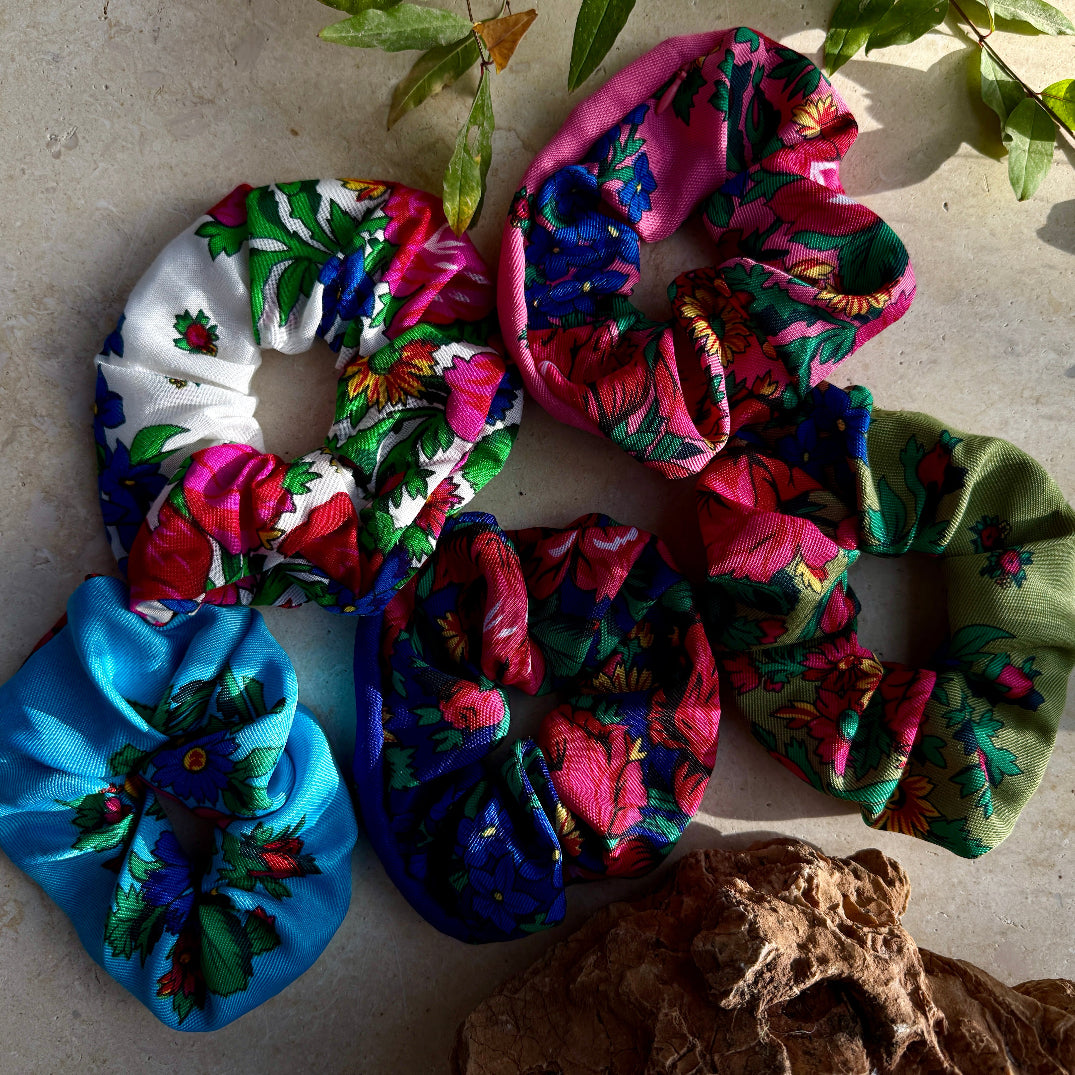 Colorful floral scrunchies on a textured surface with leaves.